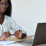 Young intelligent african American student at desk with papers and laptop.