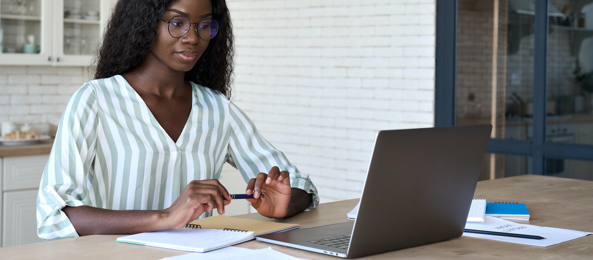 Young intelligent african American student at desk with papers and laptop.