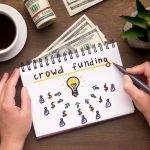 Woman hand writing in notebook crowdfunding sign on table
