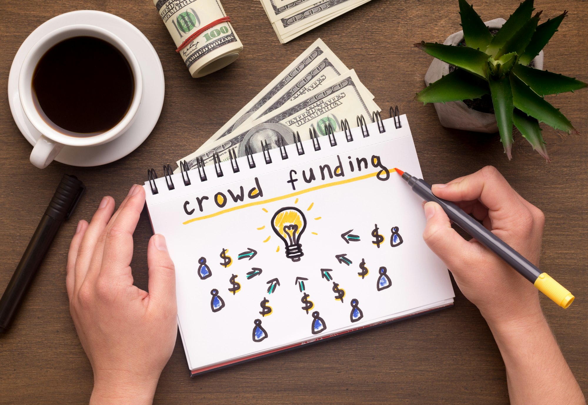 Woman hand writing in notebook crowdfunding sign on table