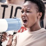 not stopping until were heard. Shot of a young woman shouting through a megaphone at a protest.