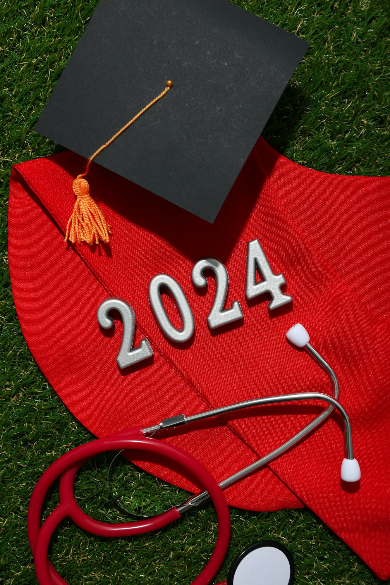 A graduate's collar and hat, with a stethoscope on the grass.