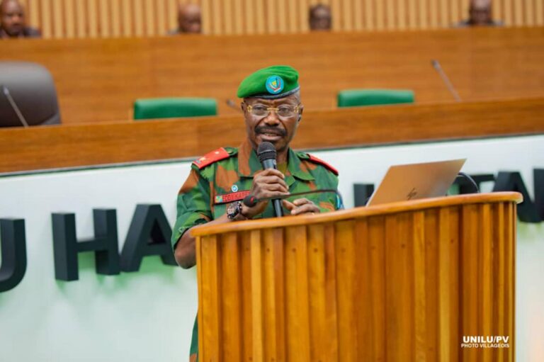 Le général Eddy Kapend, en tenue militaire et béret vert, s’exprime au micro derrière un pupitre à l’Université de Lubumbashi.