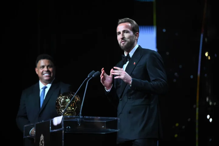 Harry Kane en costume au micro, à côté du trophée du Ballon d’Or.